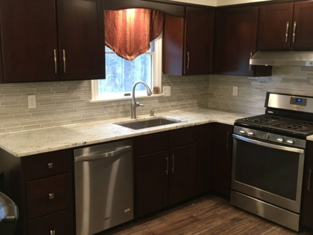 Beautiful kitchen cabinet refacing in Langhorne, PA with shaker style door and drawer fronts. The cabinetry is a cherrywood stained in a dark red wine hue. Quartz countertops, a stunning tile back splash and silver hardware wonderfully accent the new look.