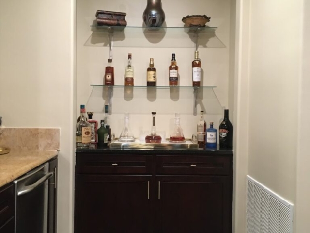 Custom bar with solid surface top and glass shelving for extra storage and display